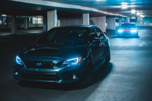 Free Gray and red autos with glowing headlights parked on asphalt on underground parking lot near stone columns Stock Photo