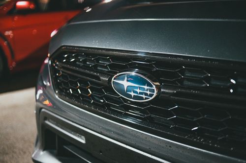 Free Bumper of modern gray automobile with logo on metal grille parked on public parking lot with red car on street Stock Photo