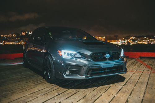 Free Expensive modern automobile with glowing headlights parked on wooden waterside near sea against cityscape with shiny buildings in evening time Stock Photo