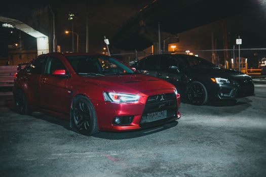 Red Mitsubishi Lancer Evo and black Subaru Impreza parked at night under city lights.