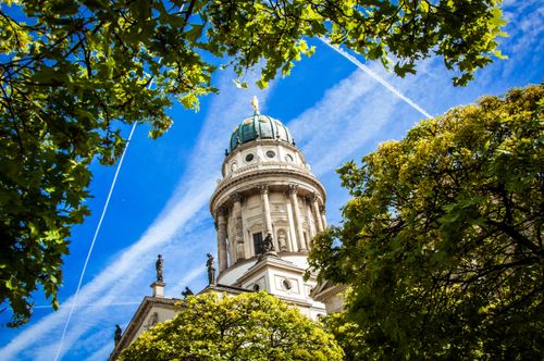 Free Bright view of Deutscher Dom in Berlin, framed by vibrant green trees. Stock Photo
