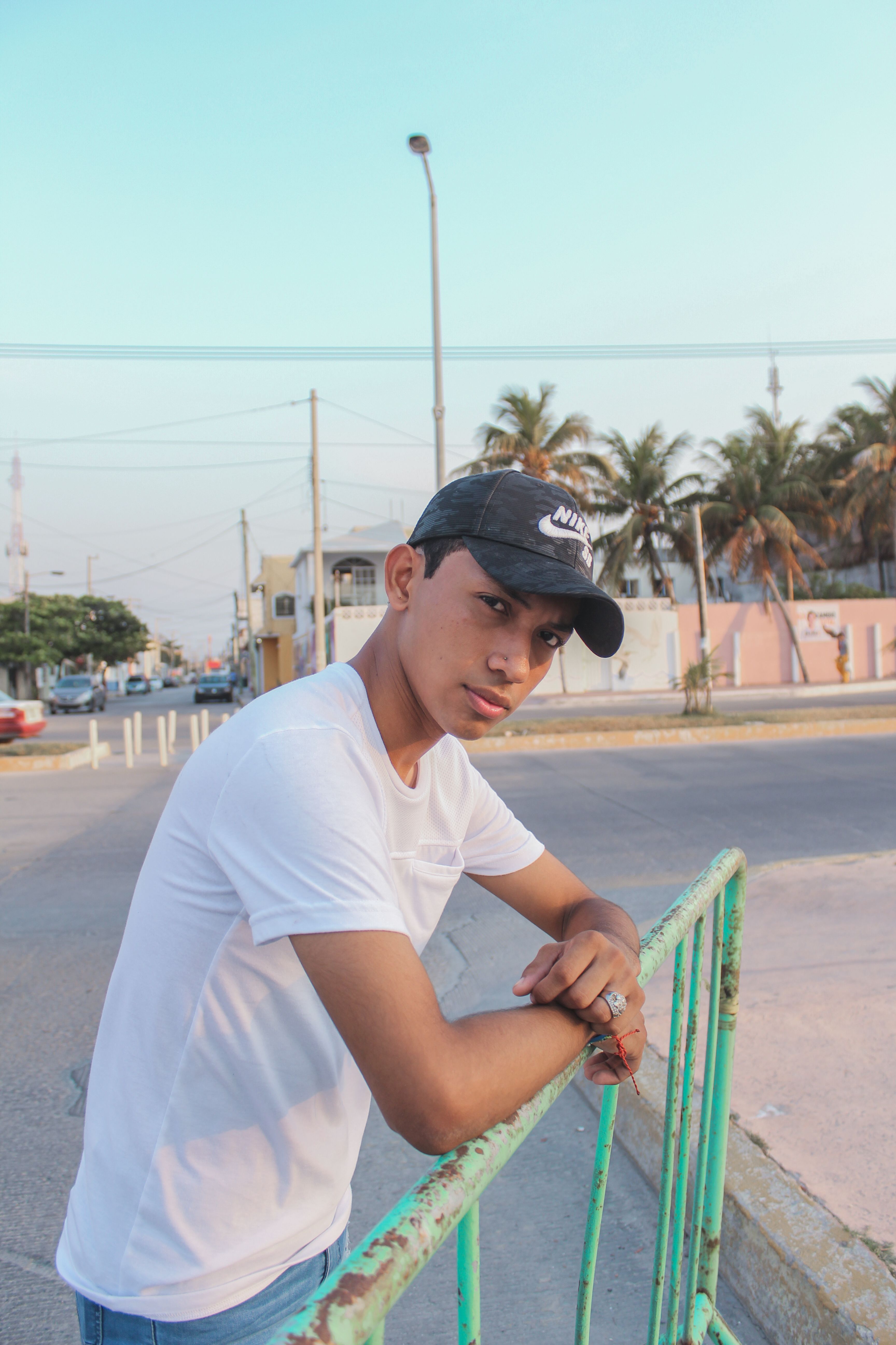 Teenage boy in casual attire leaning on a colorful fence, outdoors during daytime.