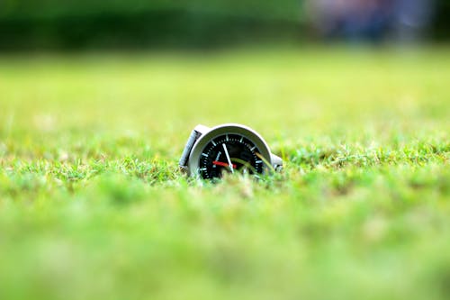 круглые серо черные аналоговые часы на зеленой траве