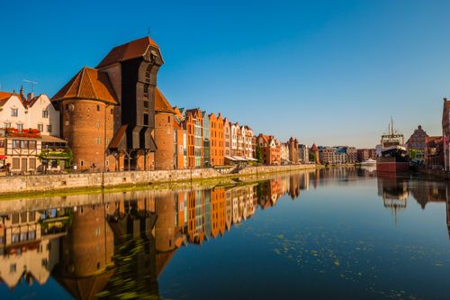 Free Beautiful view of the historic crane and waterfront buildings reflecting in the calm waters of Gdańsk, Poland. Stock Photo