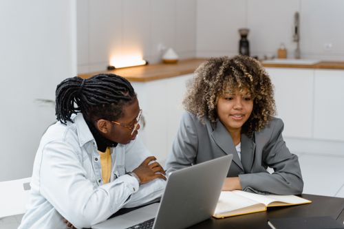 Free Two colleagues engaged in a teamwork session using a laptop and notebook in a modern workspace. Stock Photo