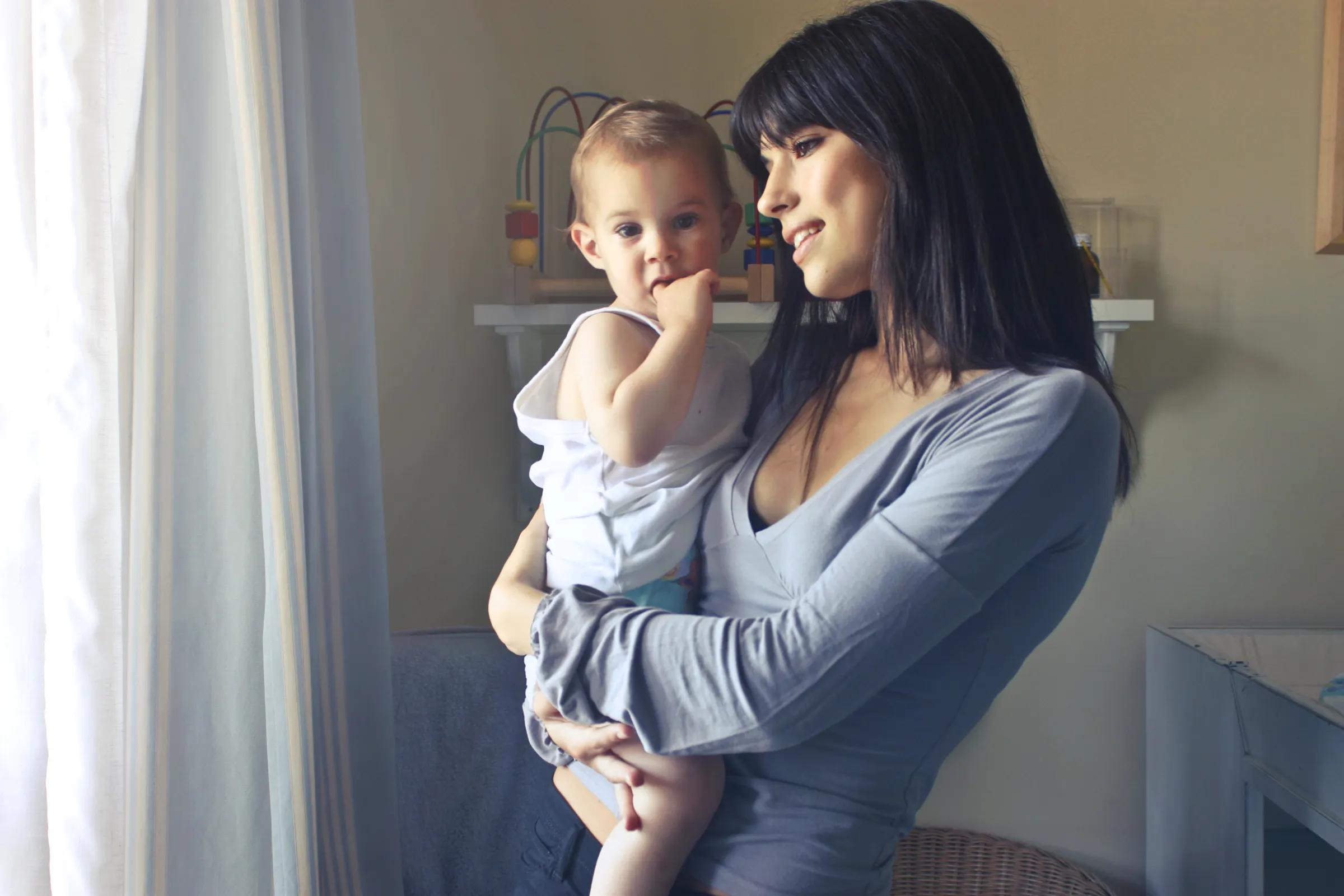 A mother holding her baby close in soft indoor light, sharing a quiet warm moment