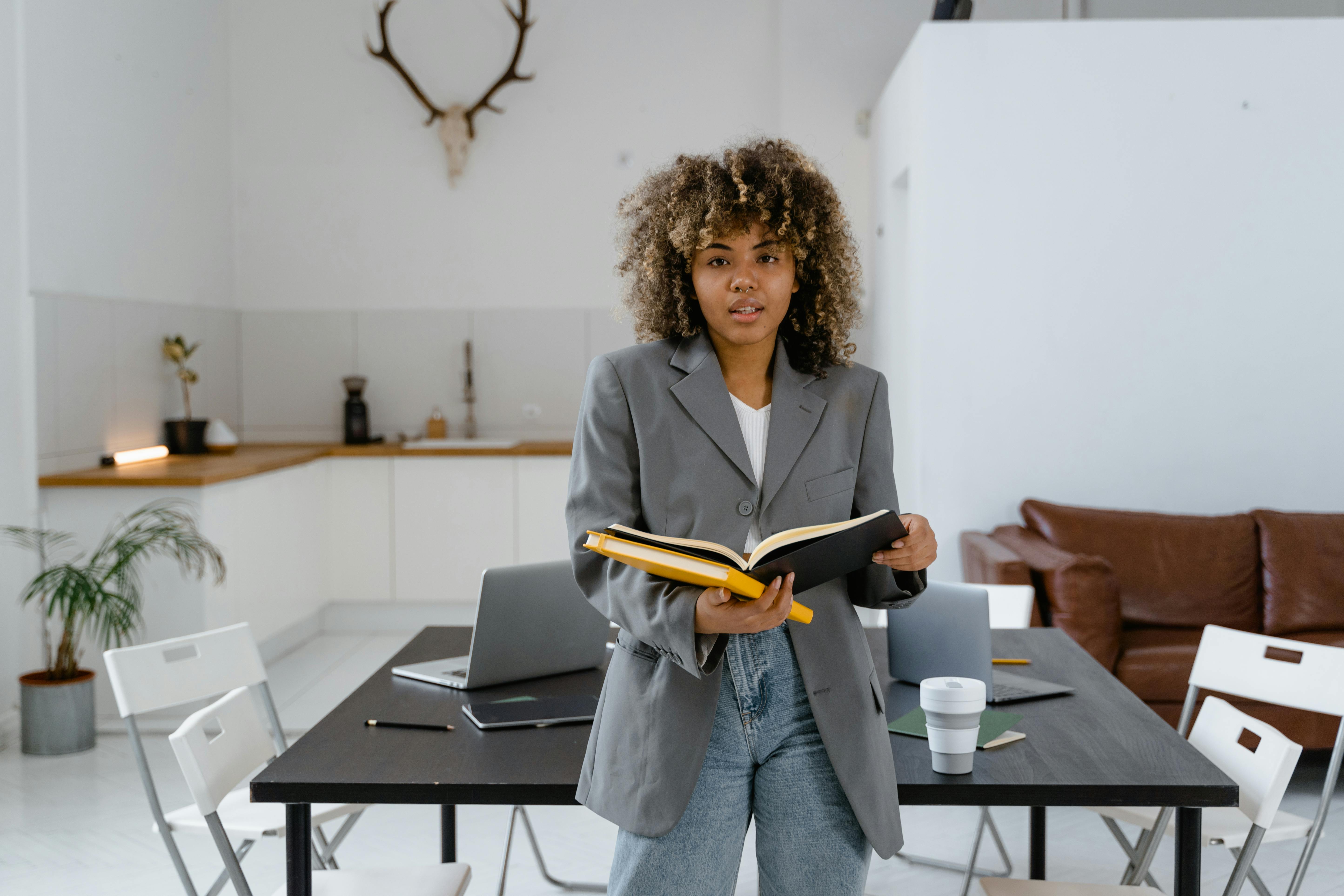Confident businesswoman in a blazer holding a book in a stylish office.