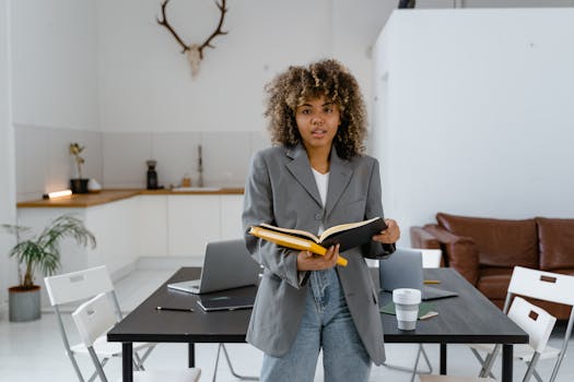 Confident businesswoman in a blazer holding a book in a stylish office.