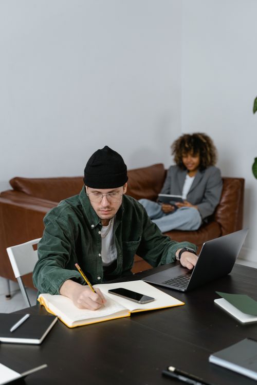 Free Two young adults working together in a minimalist office setting, focusing on tasks. Stock Photo