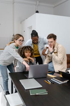 Diverse group of coworkers collaborating on a project using a laptop in a modern office.