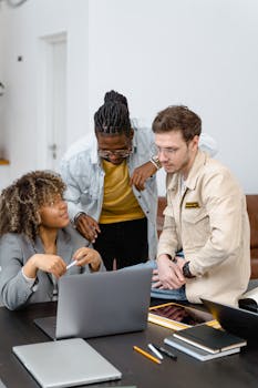 A diverse group of colleagues engaged in a collaborative project discussion around a laptop.