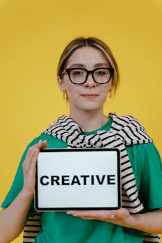 Young woman holding a tablet displaying 'Creative' on a yellow background.