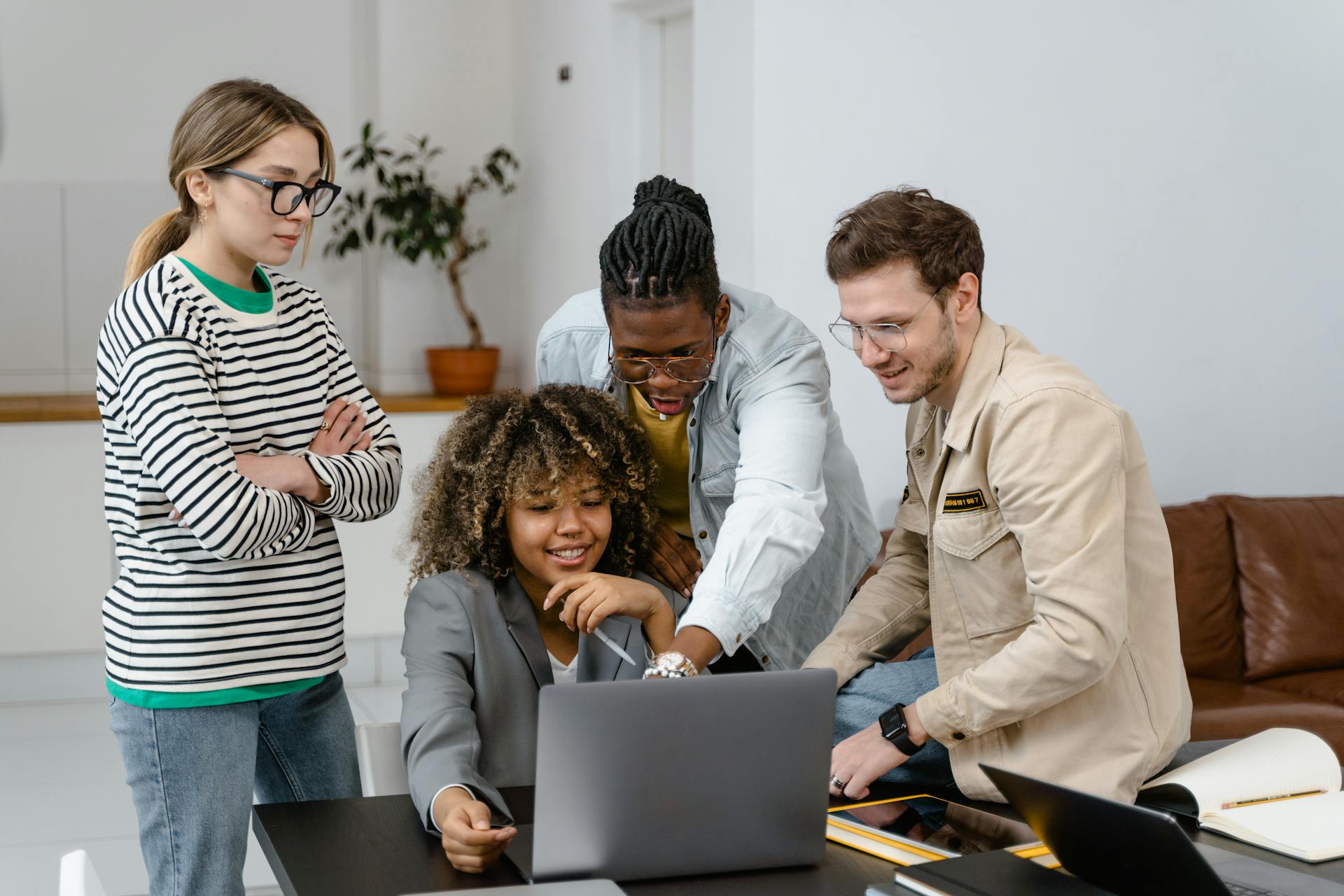 Group of diverse colleagues engaged in a team meeting around a laptop in a stylish office setting.