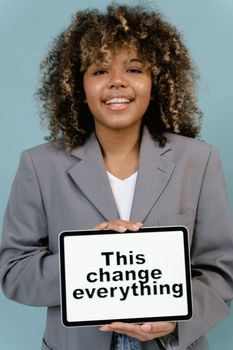 Smiling woman with afro hair holding a tablet displaying an inspiring message.
