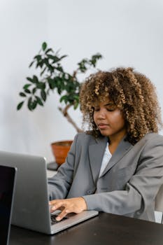 Businesswoman in gray suit focused on laptop in modern workplace.