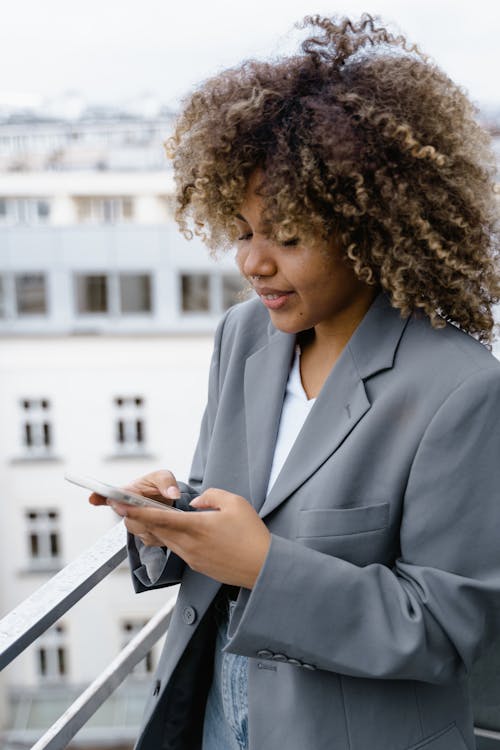 Close-Up Photo of a Woman in a Gray Blazer Using Her Cell Phone