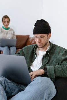 A man and woman sitting indoors using laptops, focused on remote work.