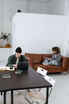 Two professionals working in a modern workspace, one on a laptop, the other on a tablet.