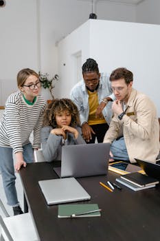 A diverse team of adults collaborating in a modern office setting with laptops and notebooks.
