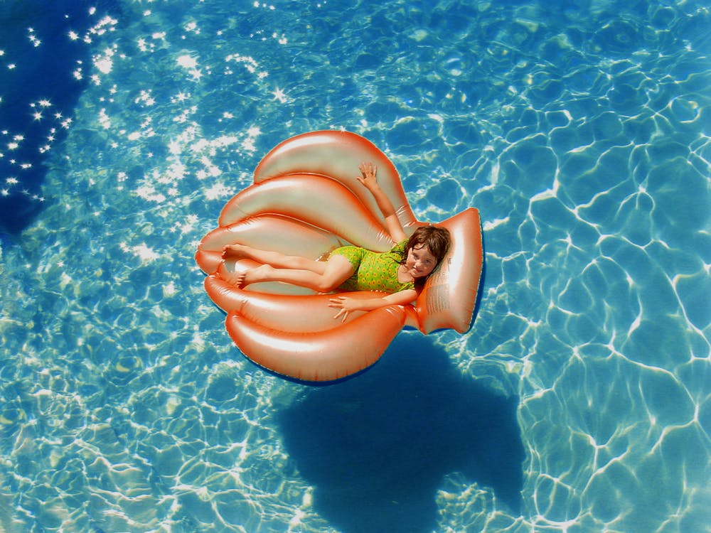 Girl Wearing Green Wet Suit Riding Inflatable Orange Life Buoy on Top of Body of Water