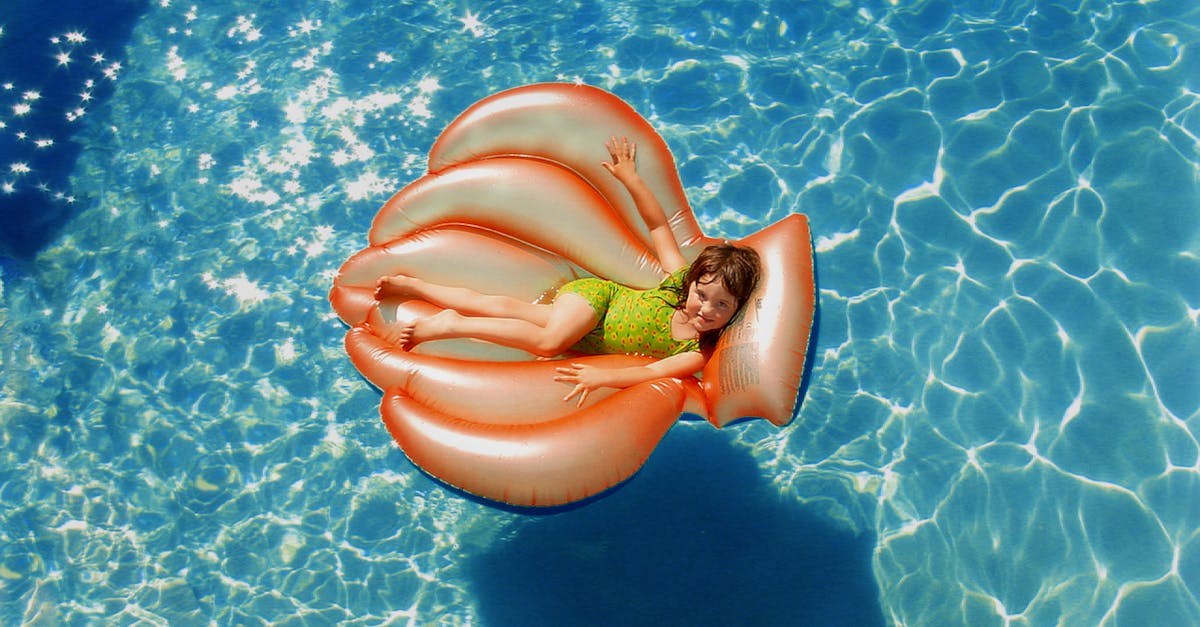 Girl Wearing Green Wet Suit Riding Inflatable Orange Life Buoy on Top of Body of Water