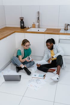 Two professionals brainstorm ideas in a kitchen space, working with documents and a laptop.