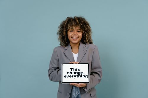 Free African American woman smiling while holding a tablet with an inspiring message, wearing a blazer. Stock Photo