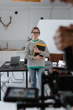 Young woman in striped sweater holding notebook in modern office with laptops and décor.
