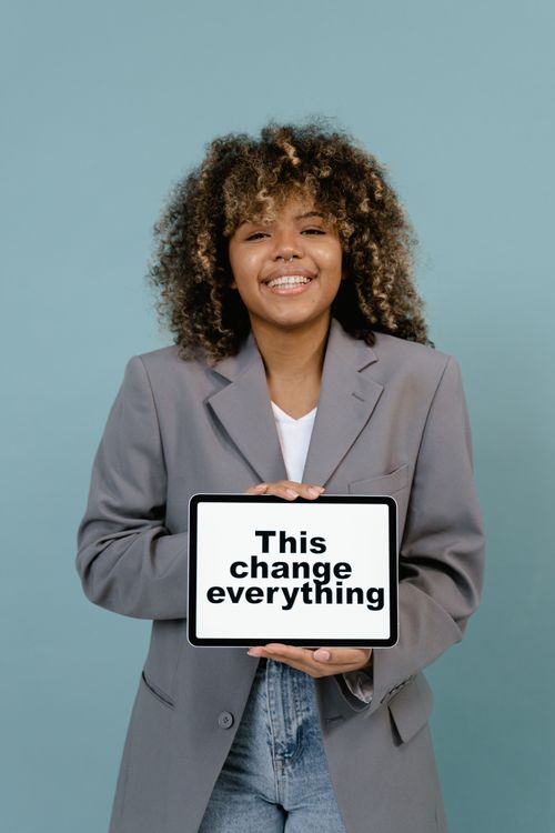 Free Young woman smiling while holding a sign that reads 'This change everything'. Stock Photo