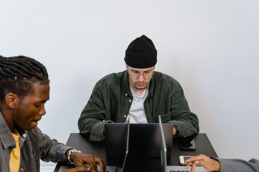 Diverse team working intently on laptops at an office. Collaborative work session depicted.