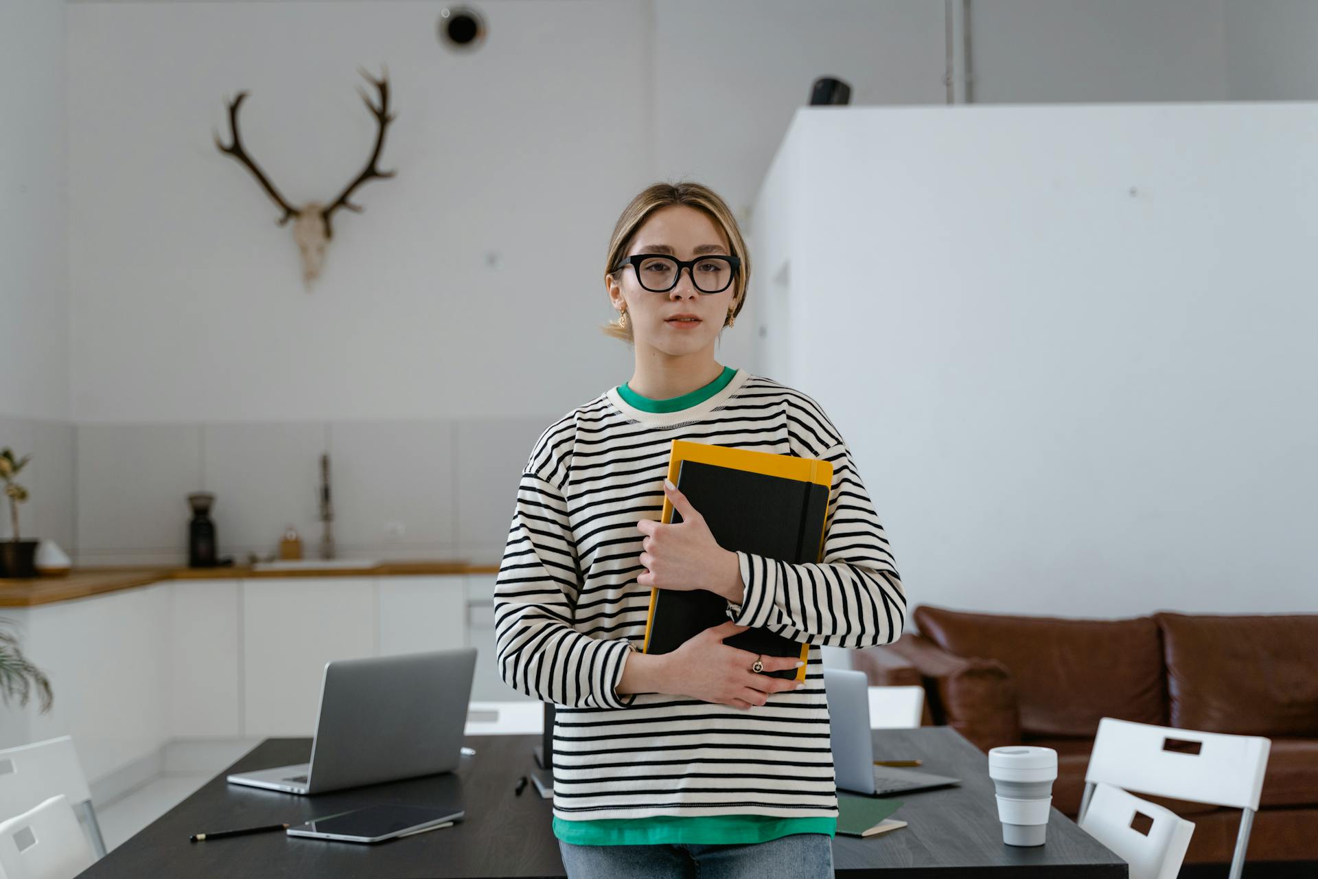 A young woman holding a folder in a contemporary office setting with a laptop.