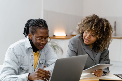 Free Two professionals discussing work on laptops and tablets in a modern office. Stock Photo