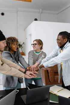 Diverse colleagues joining hands in a show of unity and teamwork in a modern office setting.