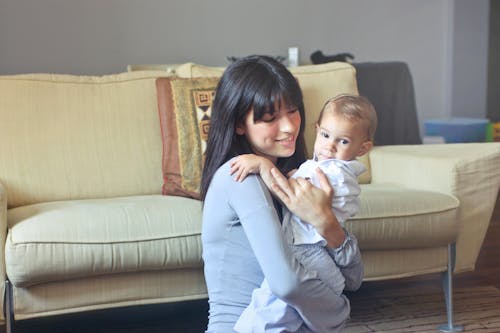 Donna In Maglione Grigio Che Trasporta Bambino In Camicia Bianca Abbottonata