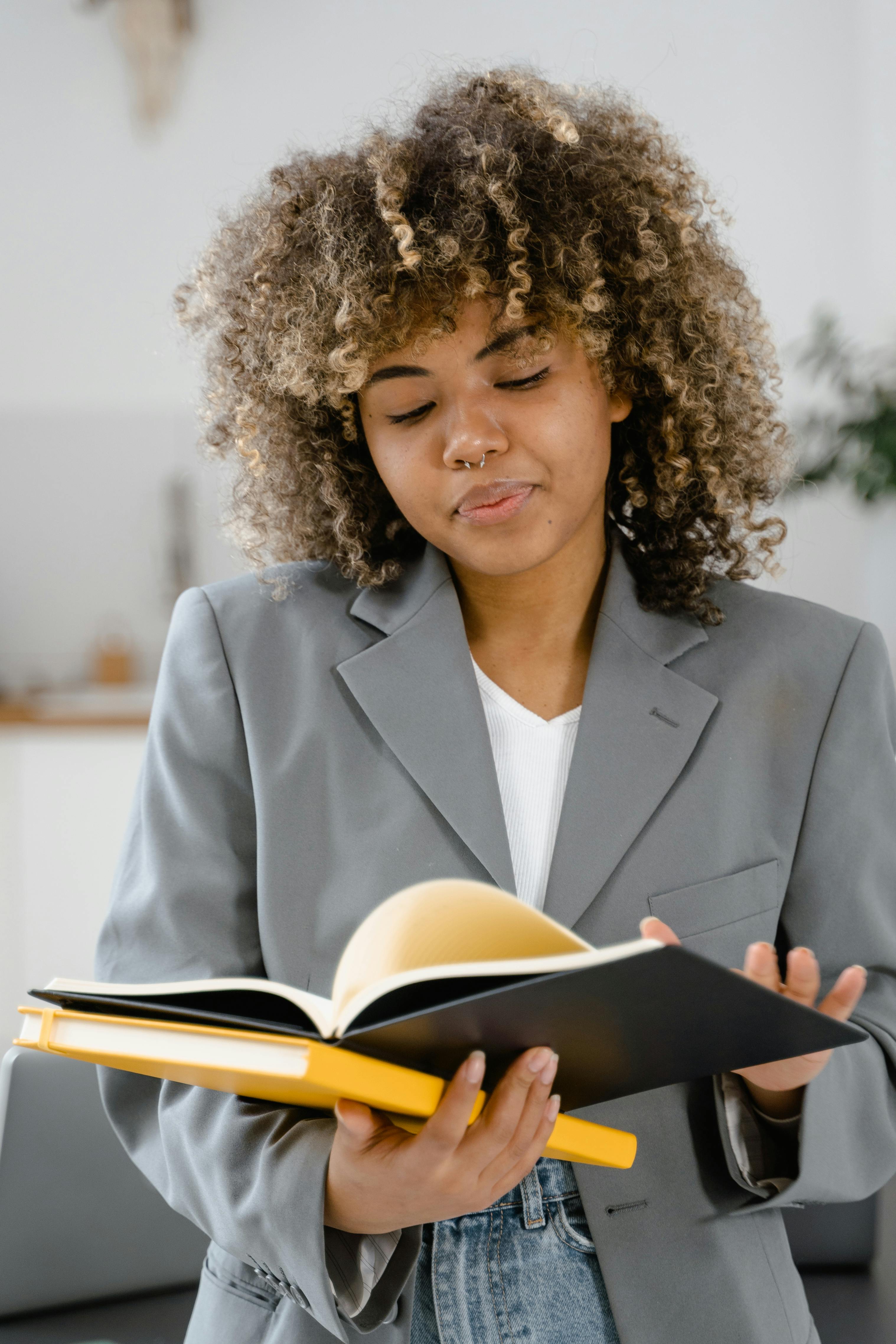 African American woman reading with focus, wearing a gray blazer indoors.