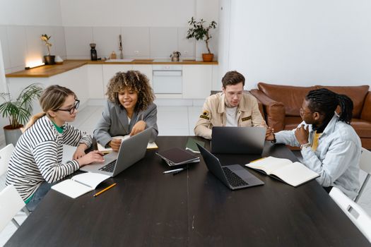 Diverse group of colleagues collaborating around a table in a contemporary office setting with laptops.