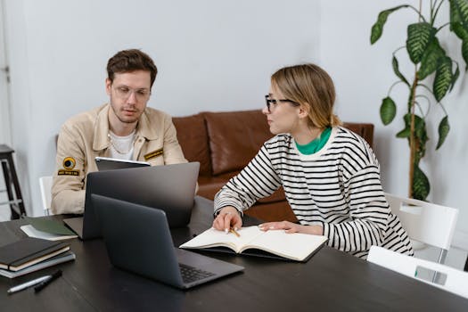 Two young professionals working together on laptops and notes in a modern office.