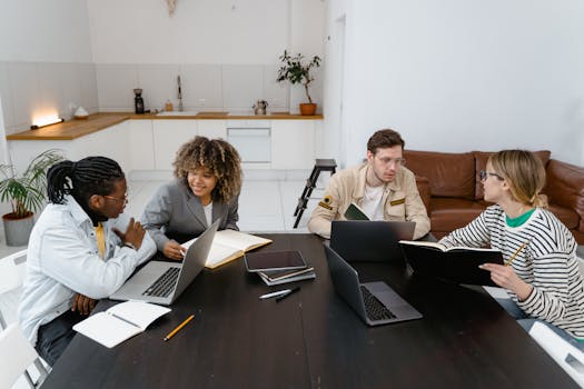 Diverse group discussing ideas with laptops and notebooks in a modern office setting.