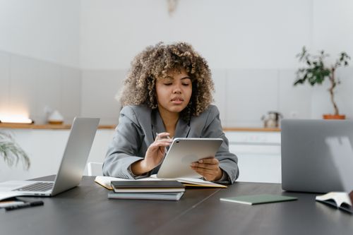Free Woman with curly hair using a tablet in a modern office setting. Stock Photo
