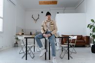 Man in Brown Jacket and Blue Denim Jeans Sitting on Chair