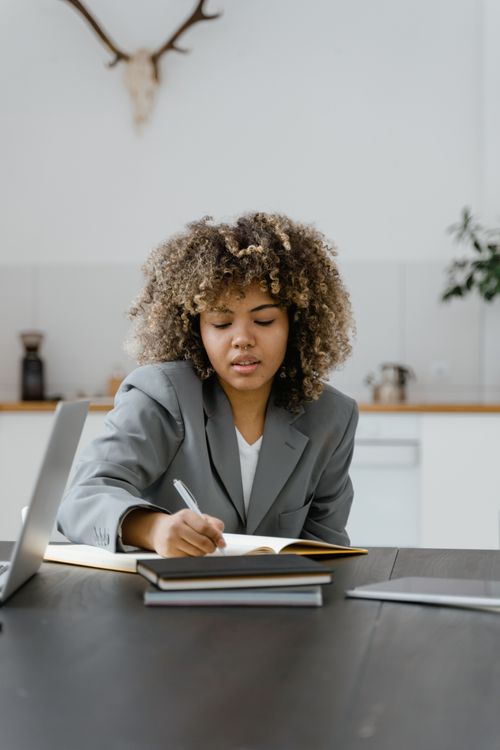 Free Adult woman with curly hair writing in a notebook in a modern office setting. Stock Photo