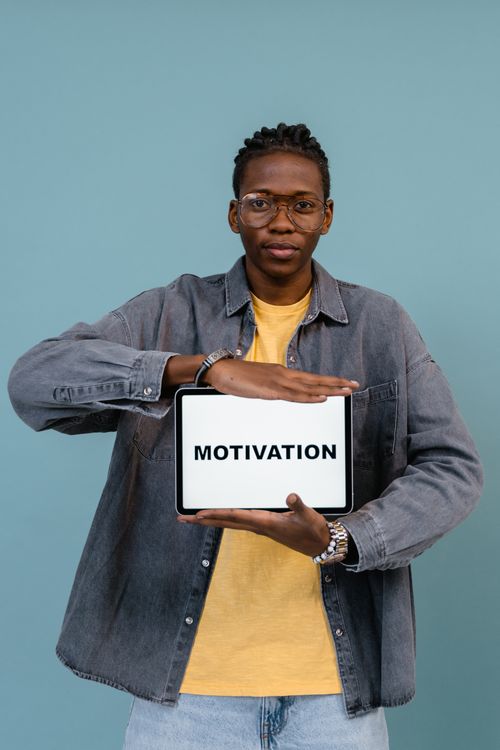 Free An African American man confidently holds a 'MOTIVATION' sign in a studio setting, inspiring positivity. Stock Photo