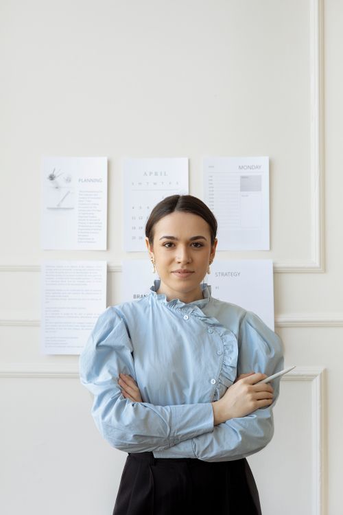 Free Professional woman in stylish attire standing in a modern office setting with crossed arms. Stock Photo