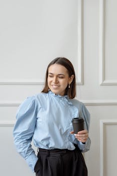 Smiling businesswoman in a blue blouse holding a disposable cup indoors.
