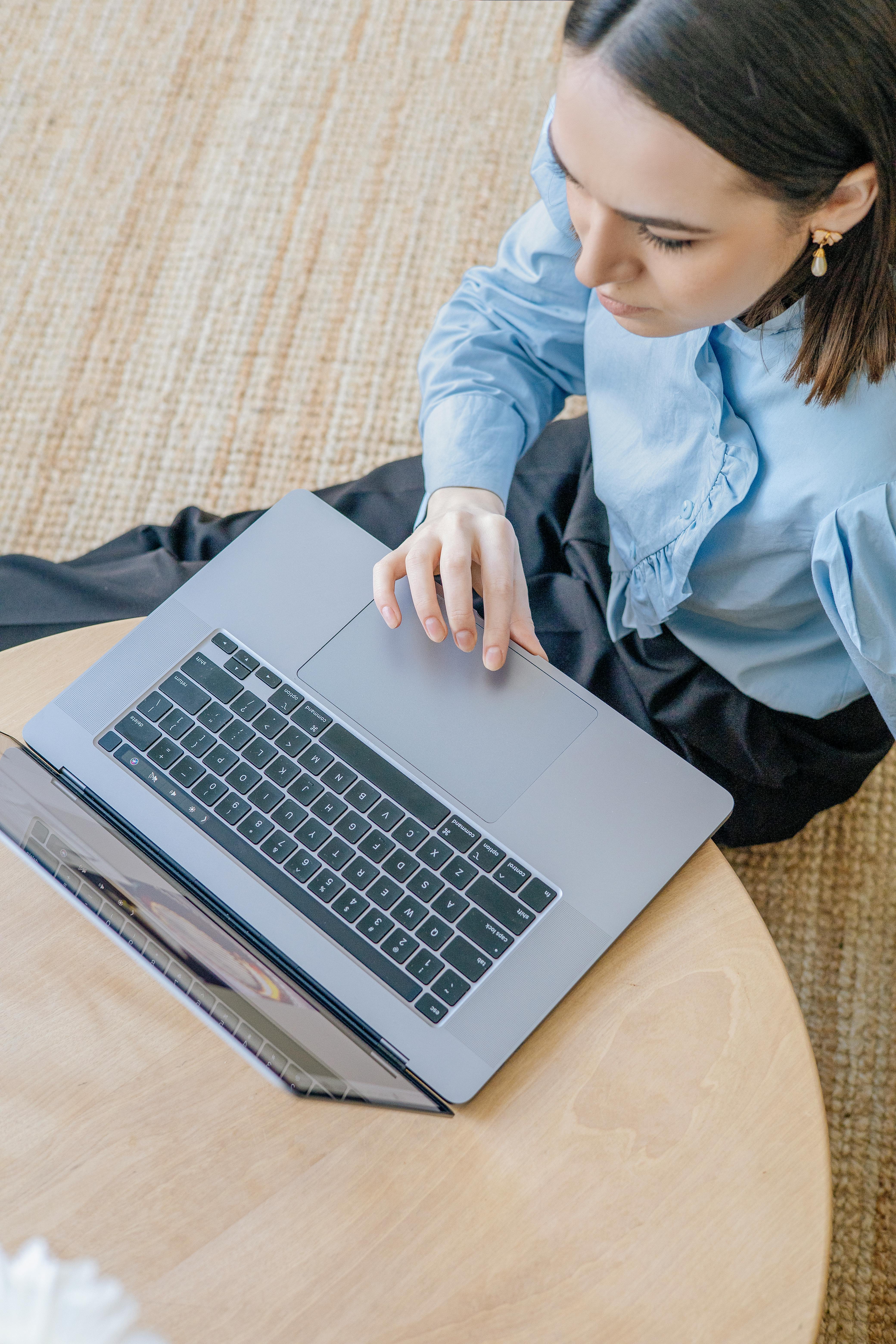 a woman in blue long sleeves sitting on the floor while using her laptop