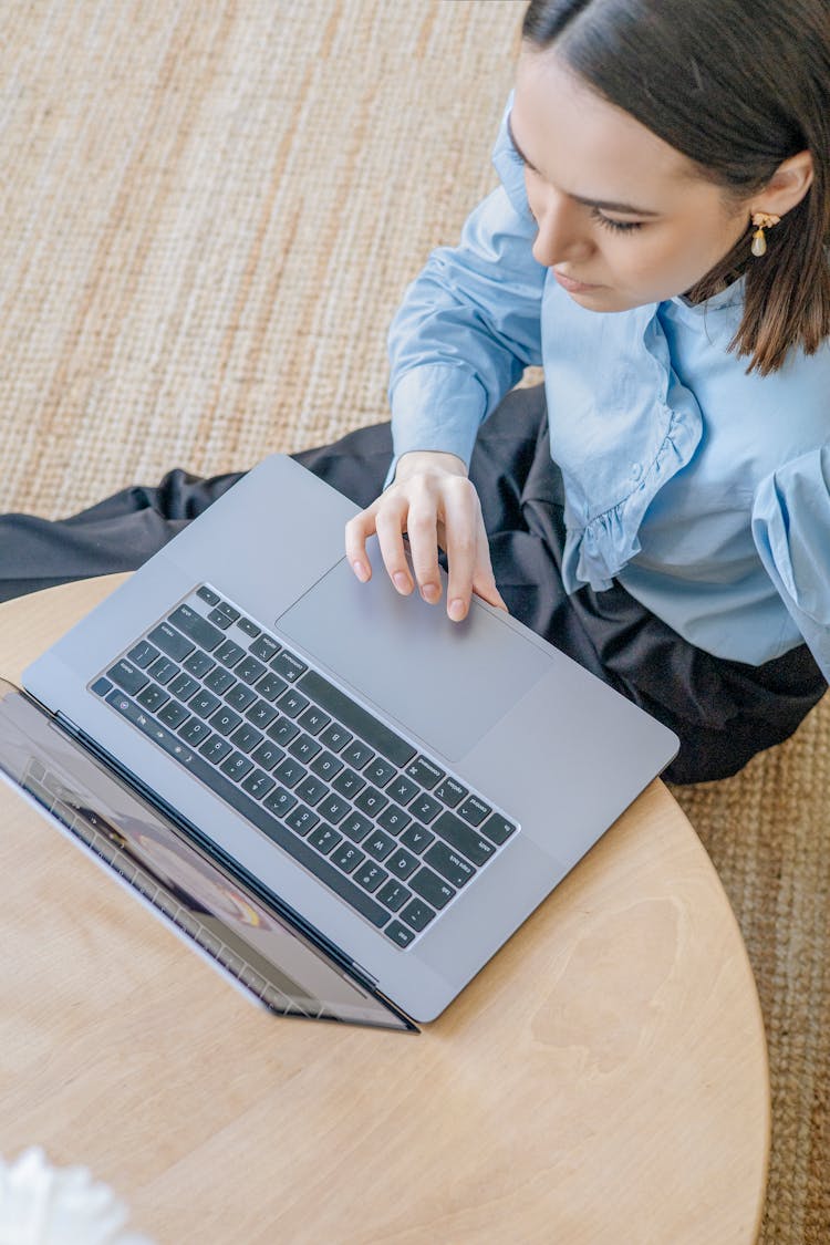 A Woman In Blue Long Sleeves Sitting On The Floor While Using Her Laptop