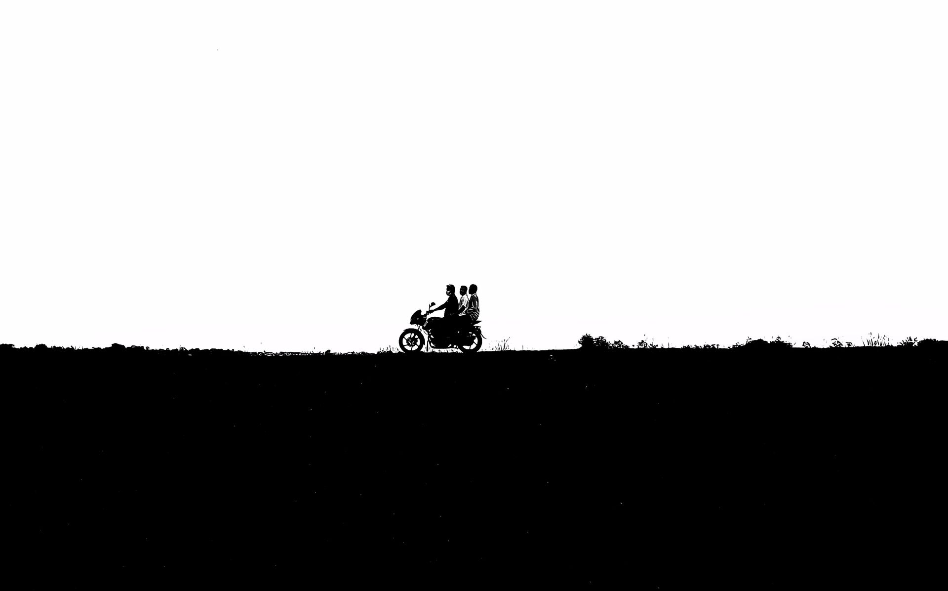 Three silhouettes riding a motorcycle against a clear sky in Gazipur, Bangladesh.