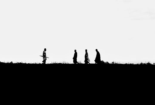 Black and white silhouette of men in traditional clothing walking on a field in Bangladesh.