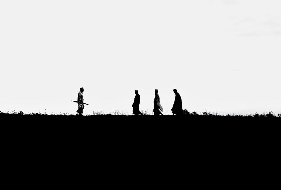 Como Superar o Medo de Morrer e Viver com Plenitude 2 Black and white silhouette of men in traditional clothing walking on a field in Bangladesh.