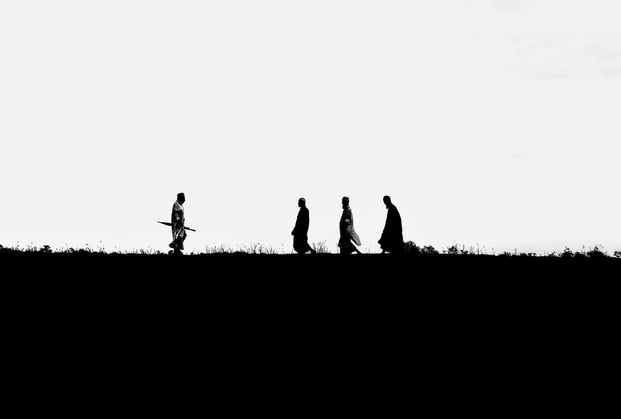 black and white silhouette of men in traditional clothing walking on a